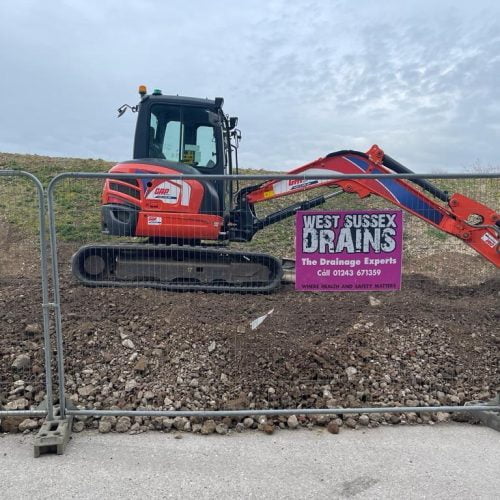 GRP digger on mound of soil behind fencing with West Sussex Drains signage to fence