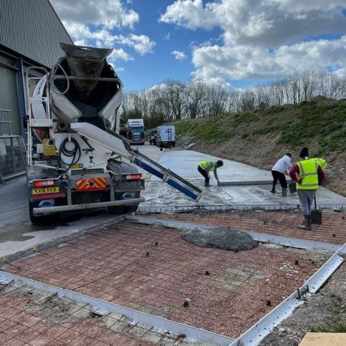 Cement truck spreading cement over area with workmen in hi vis jackets